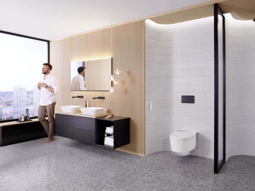 Uomo in un ampio bagno con mobili scuri e WC con funzione bidet Geberit AquaClean Uomo in un ampio bagno con mobili scuri e WC con funzione bidet Geberit AquaClean